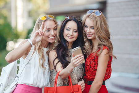 Three girlfriends looking at pictures on smartphone.Three young beautiful women, two blondes and a...