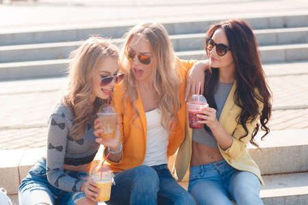 Three smiling women sitting on the steps in the Park.Three beautiful young women, two blondes and a...