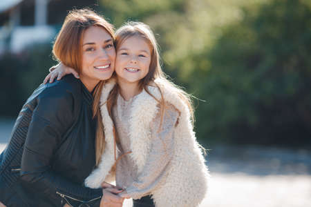 Portrait of young beautiful mom and daughter.family mother and daughter in autumn outdoors, brunette mother and daughter brunette posing on the street, hug, smile and Nestle close to each otherの写真素材