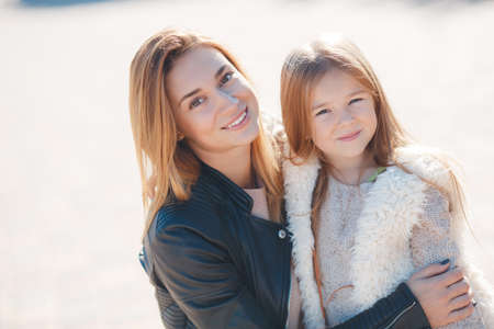 Portrait of young beautiful mom and daughter.family mother and daughter in autumn outdoors, brunette mother and daughter brunette posing on the street, hug, smile and Nestle close to each otherの写真素材