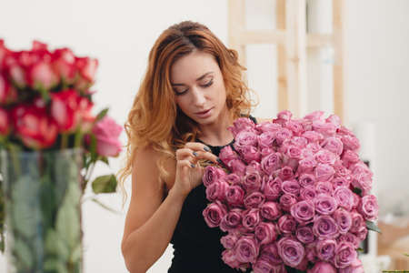 Beautiful female florist in flower shop.Beautiful business woman-the florist with long red hair, works at a flower shop on drafting of gift bouquets from fresh, beautiful flowersの写真素材