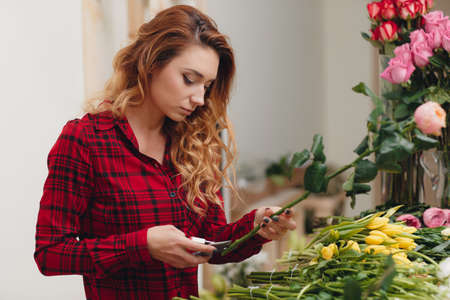 Beautiful female florist in flower shop.Beautiful business woman-the florist with long red hair, works at a flower shop on drafting of gift bouquets from fresh, beautiful flowersの写真素材