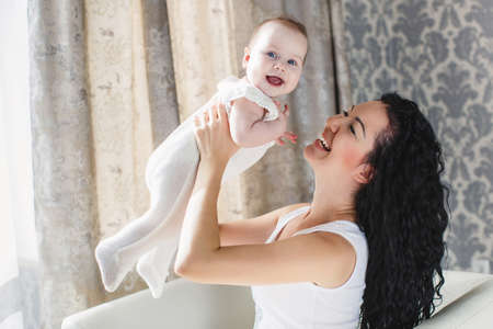 Home portrait of happy mother with a small child in her arms, a woman with long, thick black curly...