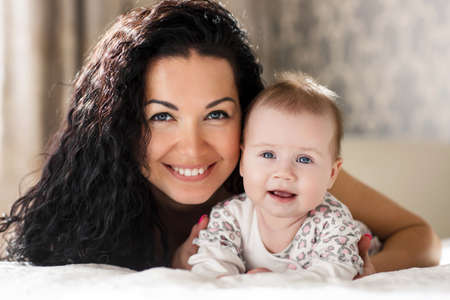 Home portrait of happy mother with a small child in her arms, a woman with long, thick black curly...