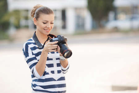 The beautiful female photographer with the digital camera.Young woman brunette in striped blouse,...