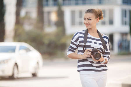 The beautiful female photographer with the digital camera.Young woman brunette in striped blouse,...