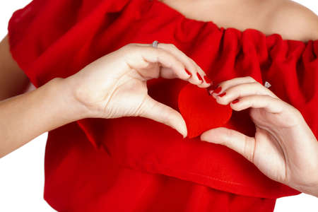 Studio portrait on white background of a beautiful young woman, brunette with blue eyes, bright red lipstick, beautiful smile, red nail Polish, dressed in a red dress, holding a red heart, Valentine's dayの写真素材