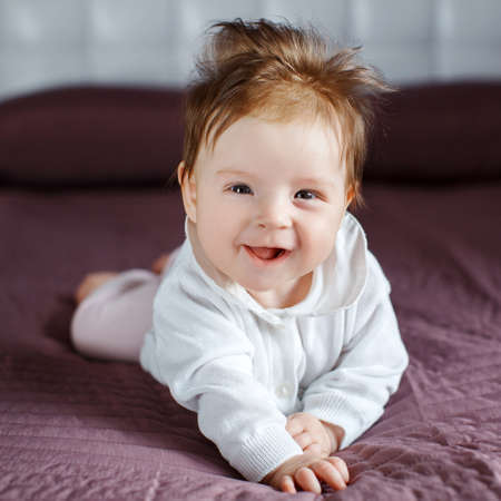 Portrait of a happy baby crawling on the bed.Little girl 3 months, brunette with brown eyes, dressed...