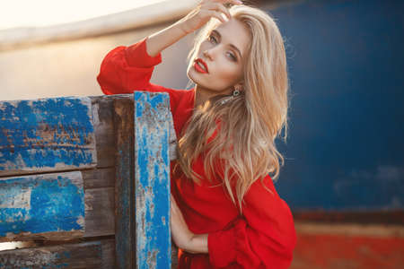 Blonde with thick long hair and grey eyes, dressed in a red dress, red lipstick, posing for the...