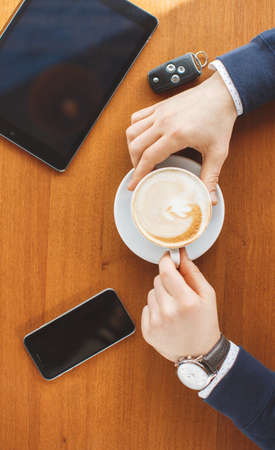 Hands of a young man on a brown table in the cafe, watch on the left hand, a Cup of cappuccino...