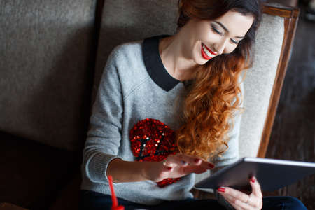 A bright, beautiful woman with curly red hair, red lipstick, beautiful makeup, red nail Polish,...