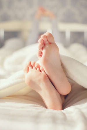 Child feet on white blanket on bed. Adorable little girl awaking up in her bed. morning. Portrait of...