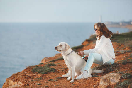 A beautiful young woman, a brunette in dark sun glasses with curly hair, dressed in a white jacket...