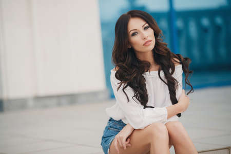 Young beautiful brunette woman with long curly hair and gray-green eyes, dressed in a white shirt...