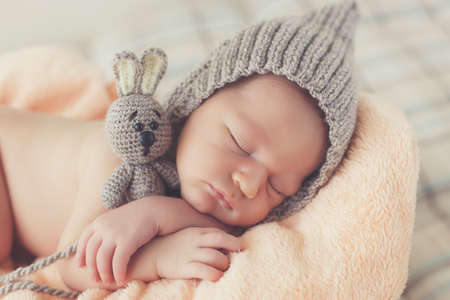 Cute girl in a gray knitted cap, put the handle under his head and hugging toy gray Bunny with big...