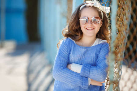 Cute teen girl, caucasian appearance, brunette with long curly hair, wearing sun glasses, wearing a blue jacket, color white ribbon tied around, spending time in the village on the football field at spring outdoor.の写真素材