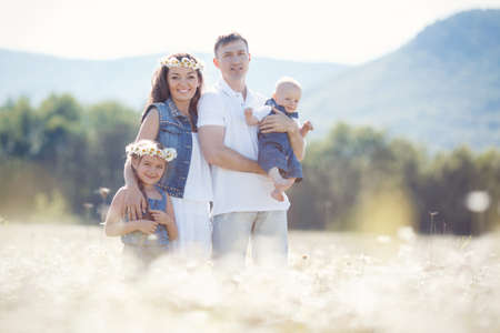 Happy family of four, mother, father, older sister and little brother spend time together in the highlands on a field of blooming white daisies in summer in the fresh air, mother and daughter wearing wreaths of flowers-white daisiesの写真素材
