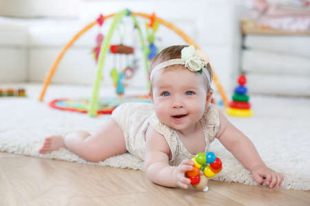 A little girl of 8 months, blonde hair tied with a white ribbon with a flower white rose, blue eyes,...