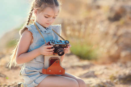 Young photographer, girl with pigtails, old camera around his neck, wearing a light summer dress, sitting on top of a cliff to take pictures of the beautiful nature, mountains and the sea, traveling aloneの写真素材