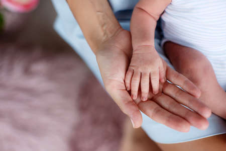 On a big, pink palm of mother, the son sitting on mother's knees has put the small pink handle, the boy is dressed in white overalls with pale blue strips, mother is dressed in a white dress, parts of a body, a hand, the concept of family happinessの写真素材