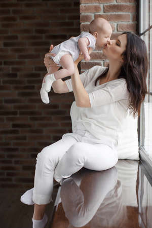Newborn baby boy with blond short hair, spends time with his mother, a woman, a brunette with long...