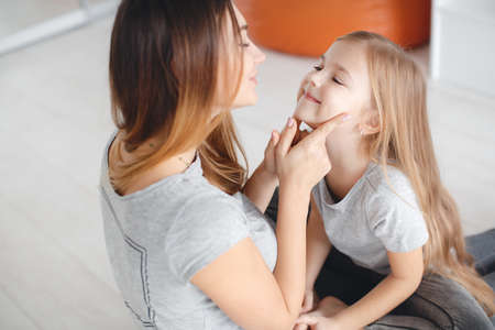 Happy mother and daughter, a woman with brown long hair, wearing jewelry, stretching her legs...