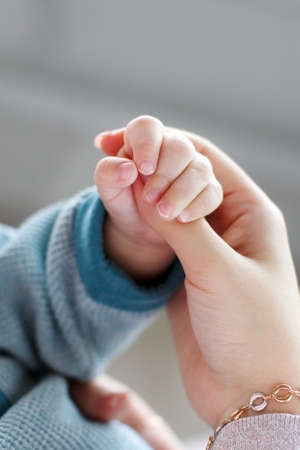 Baby holds mother's finger.A small pink pen newborn firmly holding the thumb of the hands of the mother, the baby is dressed in a knitted sweater of blue color on the wrist of the mother gold braceletの写真素材