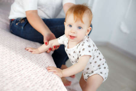Happy young mother, nails painted red nail Polish, dressed in a white blouse and blue jeans, sitting...