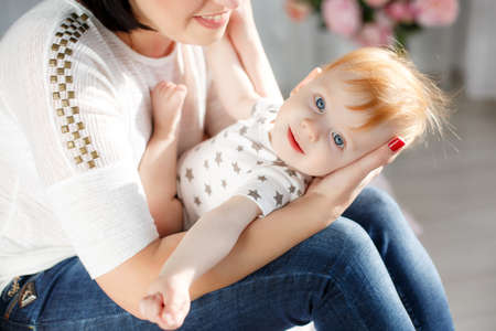 Cute young mother with thick black hair, dressed in a white T-shirt and blue jeans playing with her...