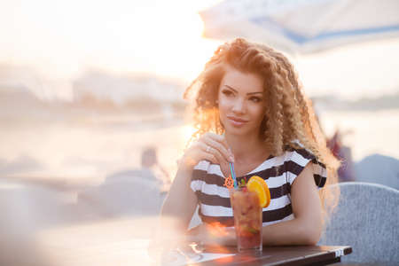 A beautiful, young woman, a brunette with long curly hair, dressed in a dark blue stripes, a sweet smile and a tempting mole on the left side of her lips, big black eyelashes and professinal make-up, posing in The summer outdoorsの写真素材