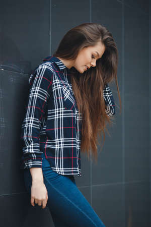 A young leader, a beautiful modern woman, a brunette with long straight hair and brown eyes, light make-up, long black eyelashes and a sweet smile, is dressed in a plaid shirt, posing standing outdoors near the mirror wall of the officeの写真素材
