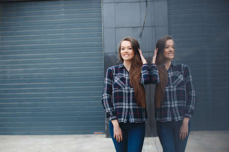 A young leader, a beautiful modern woman, a brunette with long straight hair and brown eyes, light make-up, long black eyelashes and a sweet smile, is dressed in a plaid shirt, posing standing outdoors near the mirror wall of the officeの写真素材