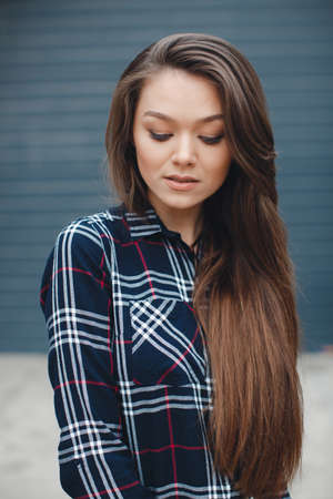 A young leader, a beautiful modern woman, a brunette with long straight hair and brown eyes, light make-up, long black eyelashes and a sweet smile, is dressed in a plaid shirt, posing standing outdoors near the mirror wall of the officeの写真素材