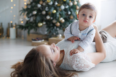 Happy family mother and little son near christmas tree on Christmas Eve at home. A woman and a...