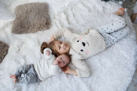 Little girl embracing a newborn baby brother. Little girl and baby boy, brother and sister playing in parents bed .Cute girl and a newborn boy resting together in a white bedroom. Family with children at home. Love, trust and tendernessの写真素材