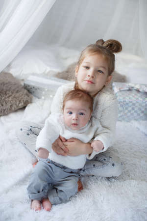 Little girl embracing a newborn baby brother. Little girl and baby boy, brother and sister playing in parents bed .Cute girl and a newborn boy resting together in a white bedroom. Family with children at home. Love, trust and tendernessの写真素材