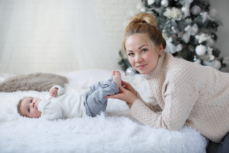 Happy young mother and her son at home during Christmas holidays. Newborn baby boy with mom indoors...