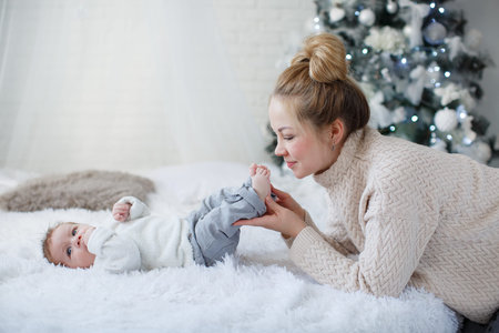 Happy young mother and her son at home during Christmas holidays. Newborn baby boy with mom indoors...