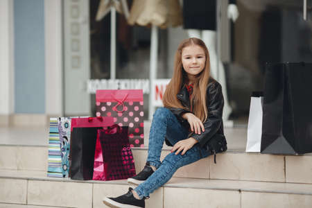 Stylish little girl with shopping bags with gifts. Happy child holds a lot of shopping bags with gifts. Black Friday sale holidays concept. Kids shoppingの写真素材