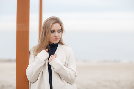Cheerful young woman by the sea.A young, beautiful woman, blonde with long straight hair and blue eyes, a cute smile and even white teeth, dressed in a knitted sweater, spends her time alone on a sandy beach near the blue ocean in early springの写真素材