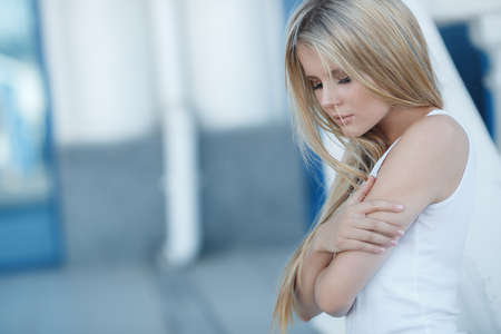 Young beautiful woman, blonde with long straight hair, dressed in a white tank top, gray-blue eyes and light make-up, posing outdoors in the summer, strolling alone through a light city in the daytimeの写真素材