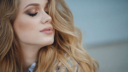 Beautiful young woman with long, thick, wavy hair, multi-colored make-up, long black eyelashes, plump pink lips, posing in studio on a blue background, portrait of a cute woman with an elegant hairstyle and perfect make-upの写真素材