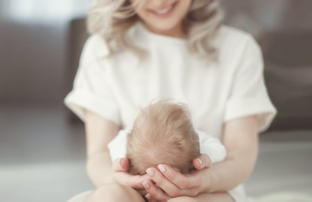 Young mother holding her newborn child. Woman and new born boy relax in a white bedroom. A young...
