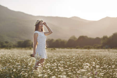Beautiful girl outdoors with a bouquet of flowers in a field of white daisies, enjoying nature. Beautiful model with long hair in white dress with fun on summer Field with blooming flowers, Sun Light. Free Happy Woman on spring meadow, countrysideの写真素材