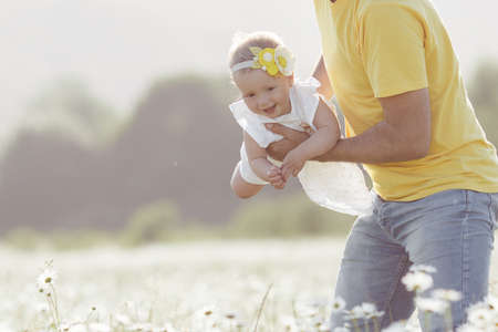 Happy young father having fun with newborn baby daughter in white chamomile field on warm summer day, family portrait together. Dad with baby girl outdoors, love. Bonding, family, new lifeの写真素材