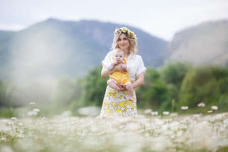 Woman holding a newborn son outdoors in the highlands  blooming chamomile field.の写真素材