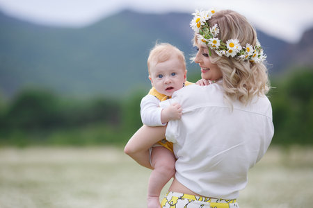 A newborn son is standing outdoors in the highlands among a blooming chamomile field. Blue sky and white meadows of blooming daisiesの写真素材