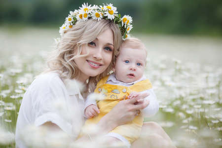 A newborn son is standing outdoors in the highlands among a blooming chamomile field. Blue sky and white meadows of blooming daisiesの写真素材