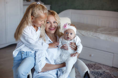Mother and Baby smiling together. Love Mom and two daughters kissing and hugging at home. Beautiful healthy mother and little daughter. Maternity concept. Parenthood. Motherhood. Mom and kidsの写真素材