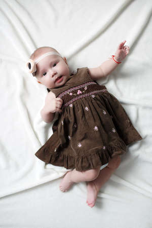 Cute adorable baby girl flying alone dressed on a white bed.Little child looking at the camera. Baby fashion clothes.の写真素材